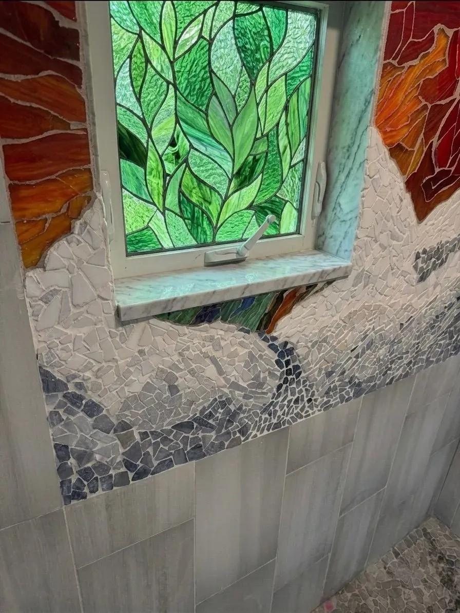 Mountain landscape mosaic framing a stained-glass window in a tiled shower